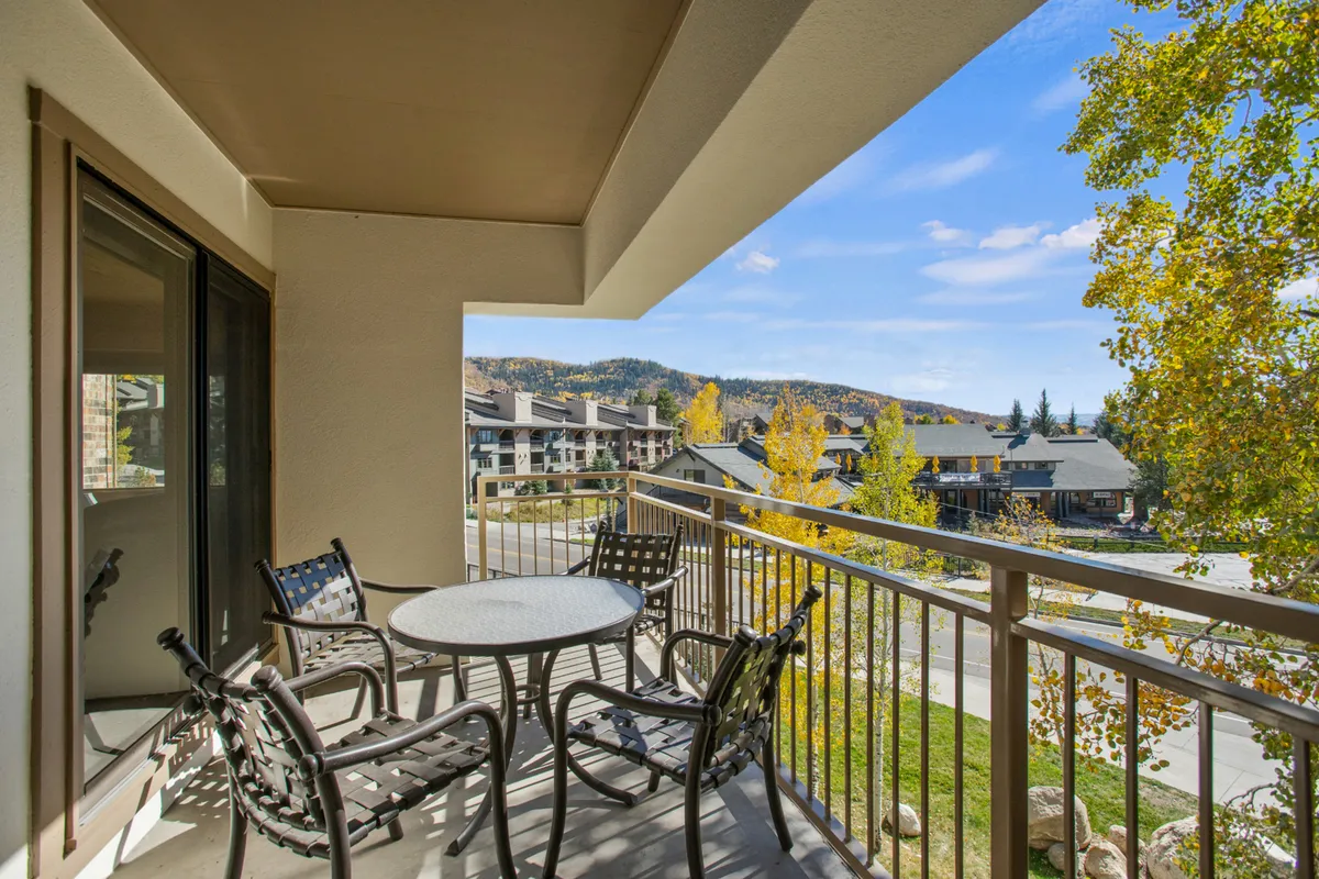 A spacious covered balcony furnished with comfortable seating, set against a backdrop of mountain views and colorful autumn foliage. The area looks perfect for relaxing with a drink and soaking in the scenery.