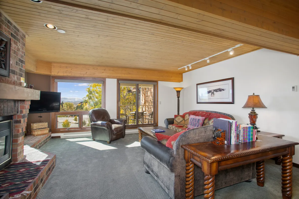 A cozy, inviting interior living room with a fireplace, large windows showcasing mountain views, comfortable seating, and a wooden table—ideal for relaxing, socializing, and unwinding after outdoor adventures.