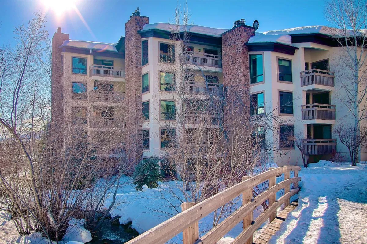 Taken in winter, this exterior shows the Dulany building with a snow-covered ground and a wooden bridge, set against a serene backdrop. The scene is tranquil, highlighting the property's close proximity to winter activities and the slopes.