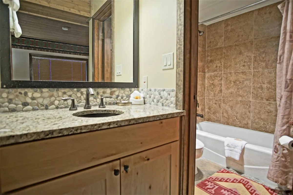 A tranquil bathroom with a granite countertop, elegant mirror, bathtub, and wooden cabinetry. The space is serene and well-appointed for both relaxation and daily routines.