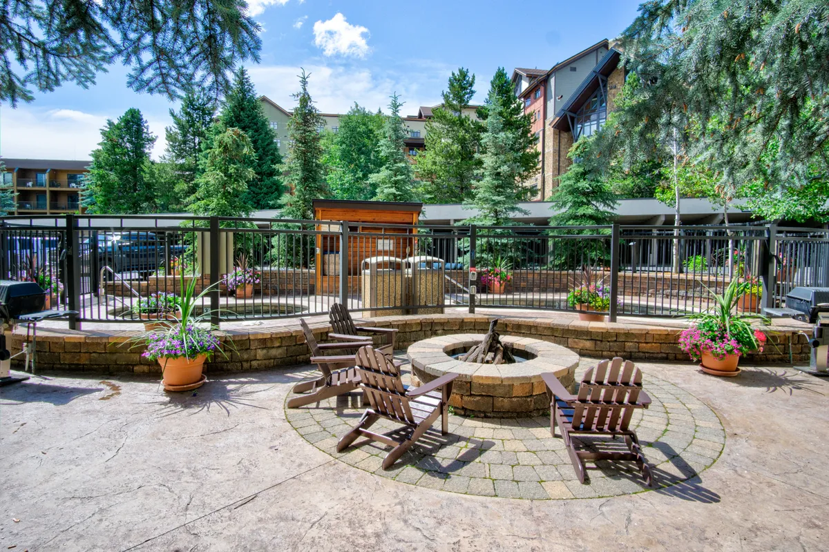 This exterior shot features a cozy fire pit surrounded by wooden chairs, lush greenery, and a stone pathway, evoking scenes of communal gatherings and relaxation outdoors. The space is inviting for evening family time, roasting marshmallows, or sharing stories after a day of adventure.